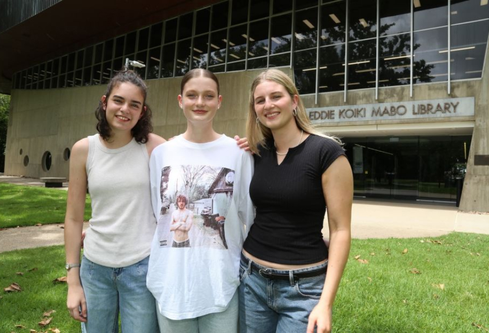 Three girls smiling and standing in front of Eddie Koiki Mabo Library